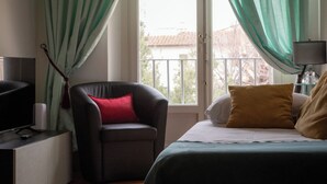 Una habitación con una cama, una silla, un televisor y una ventana con cortinas.