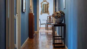Un pasillo con suelo de madera, un candelabro y un espejo con marco decorativo.