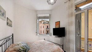 A bedroom with a bed, a television, a window with a view of buildings, and a door to a balcony. - Room 'Stanza Per 2 Persone' with Balcony and Wi-Fi (Genova)
