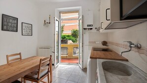 Une cuisine avec une table et des chaises en bois, un évier et une vue sur l’extérieur, accessible par une porte ouverte.