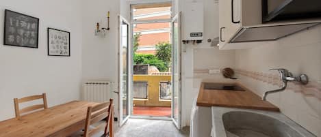 A kitchen with a wooden table and chairs, a sink, and a view through an open door to the outside.
