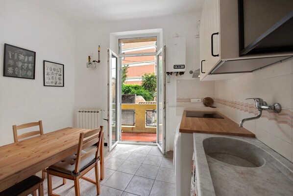 A kitchen with a wooden table and chairs, a sink, and a view through an open door to the outside.