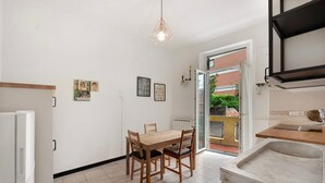 Une cuisine avec une table à manger, des chaises, un luminaire suspendu et une vue sur l’extérieur par une porte ouverte.