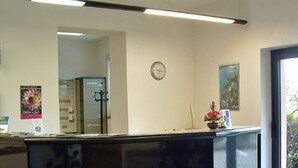 Un comptoir d’accueil avec une horloge au mur, une plante en pot et une affiche.