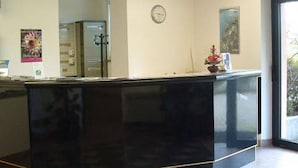 A reception area with a black reception desk, a clock on the wall, and a window with a view of greenery outside.