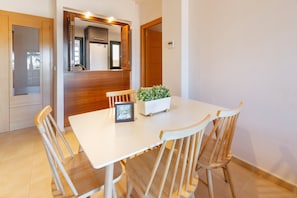 Un coin repas avec une table blanche, des chaises en bois, une petite plante en pot et un panneau décoratif encadré.