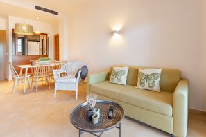 Un salon avec un canapé, un coin repas avec des chaises, une table avec une télécommande et un luminaire fixé au mur.