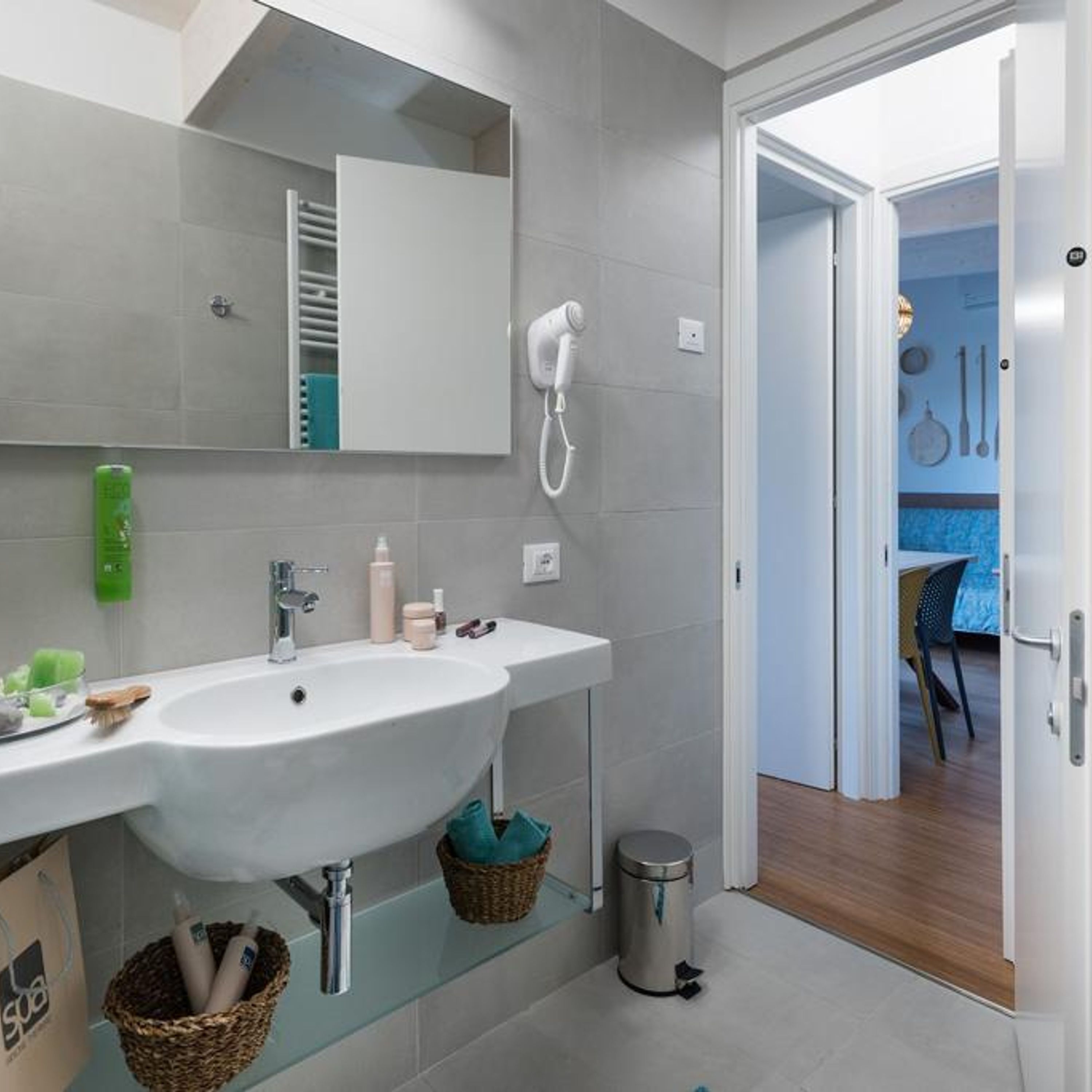 A modern bathroom with a large sink, a mirror, a hairdryer, and a trash bin.