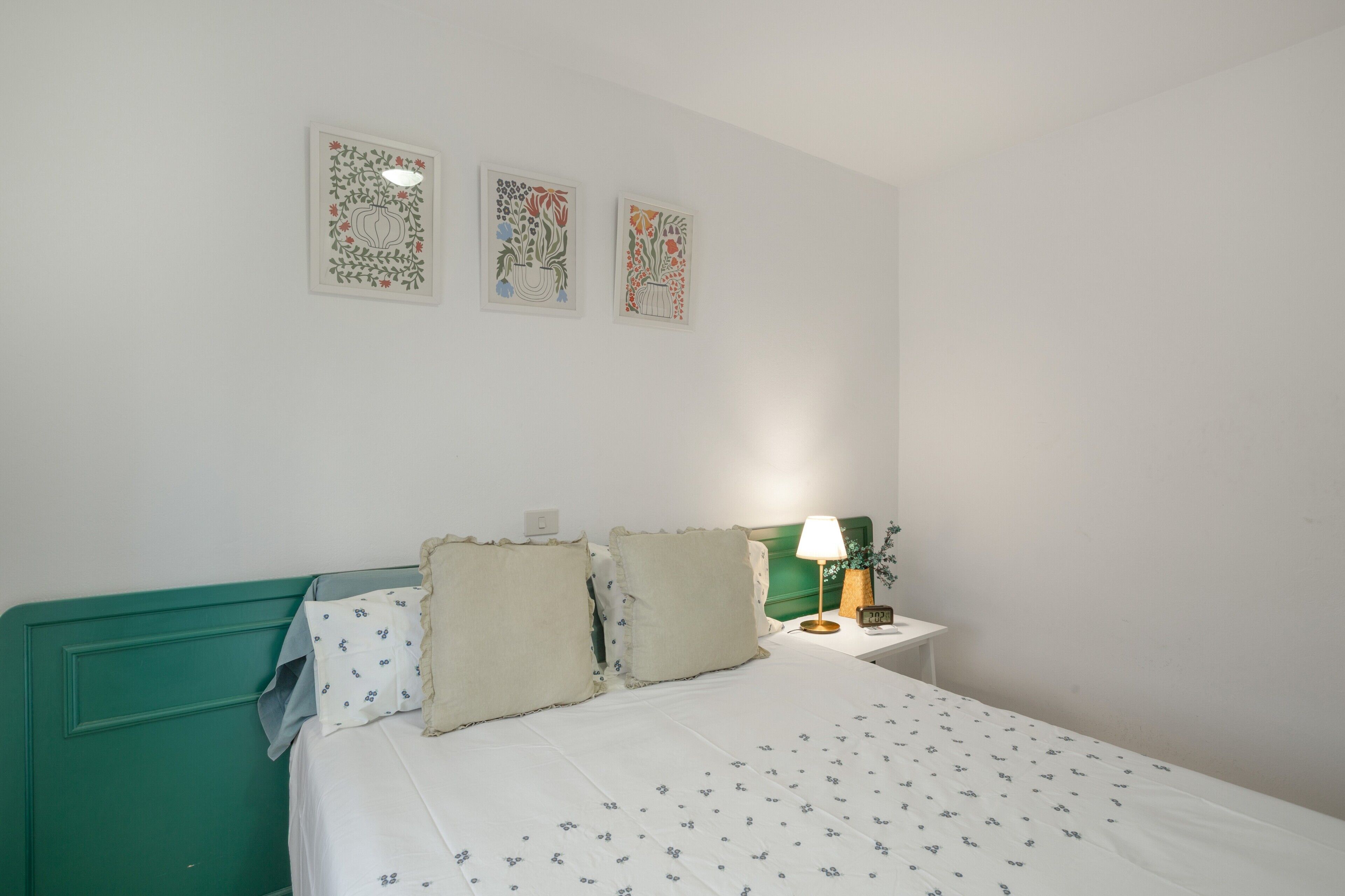 Un dormitorio ordenado con cama, almohadas, mesita de noche, lámpara y decoración en la pared.