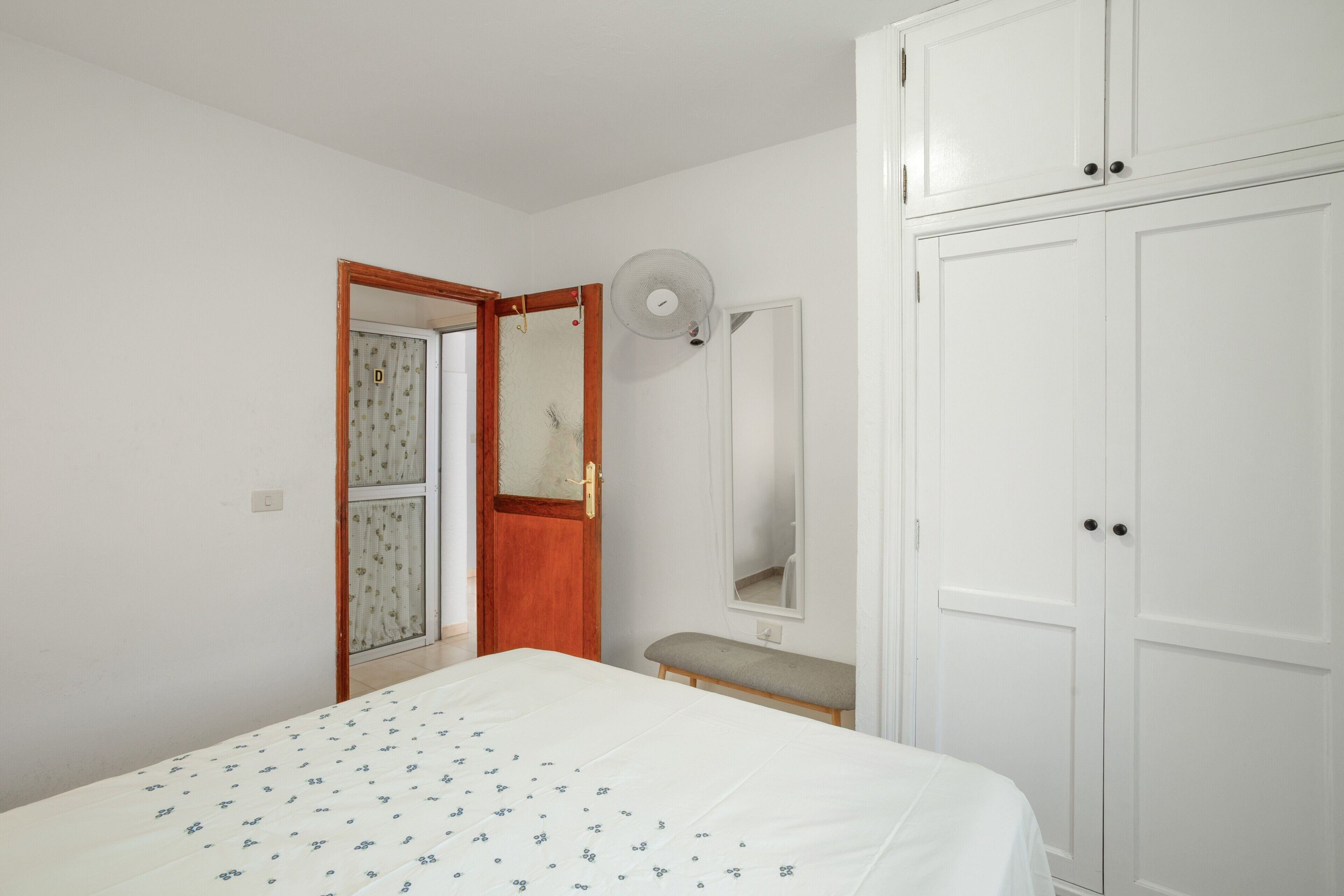 A bedroom with a bed, a wardrobe, a bench, a door, and a mirror.
