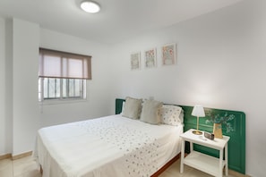 A bedroom with a bed, a bedside table with a lamp, a window with blinds, and three wall art pieces.