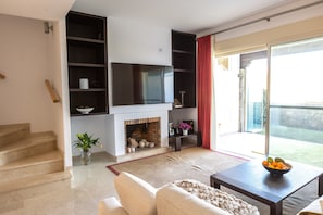 A living room with a fireplace, a flat-screen TV, a sofa, a coffee table, and a view of the outdoors.
