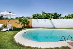 A swimming pool with a white border, a white wall, and a clear blue sky.