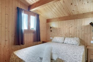 A wooden-paneled room with a bed, curtains, a bedside lamp, and a nightstand. - Holiday Home 'Casa El Mirlo' with Private Pool, Wi-Fi and Air Conditioning (Conil de la Frontera)