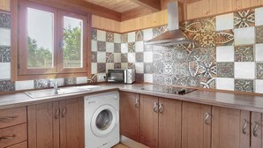 A kitchen with wooden cabinets, a washing machine, a microwave, and a patterned backsplash. - Holiday Home 'Casa El Mirlo' with Private Pool, Wi-Fi and Air Conditioning (Conil de la Frontera)