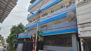 A multi-story building with a blue and white facade, a black car parked in front, and a motorcycle on the street. - Kost Griya Marina by Ecommerceloka (Jakarta)