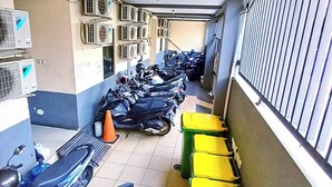 A narrow corridor with air conditioning units, a row of parked motorcycles, and trash bins. - Kost Griya Marina by Ecommerceloka (Jakarta)