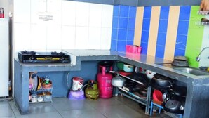 A compact kitchen with a gas stove, shelves with pots and pans, and a tiled backsplash. - Kost Griya Marina by Ecommerceloka (Jakarta)