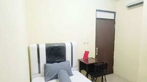 A small, simple room with a bed, a desk, and a door. - Kost Griya Marina by Ecommerceloka (Jakarta)