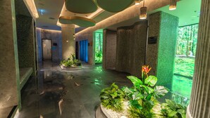 Een moderne binnenruimte met een centraal waterpartij, omringd door groen en een uitzicht op een bos door grote ramen.