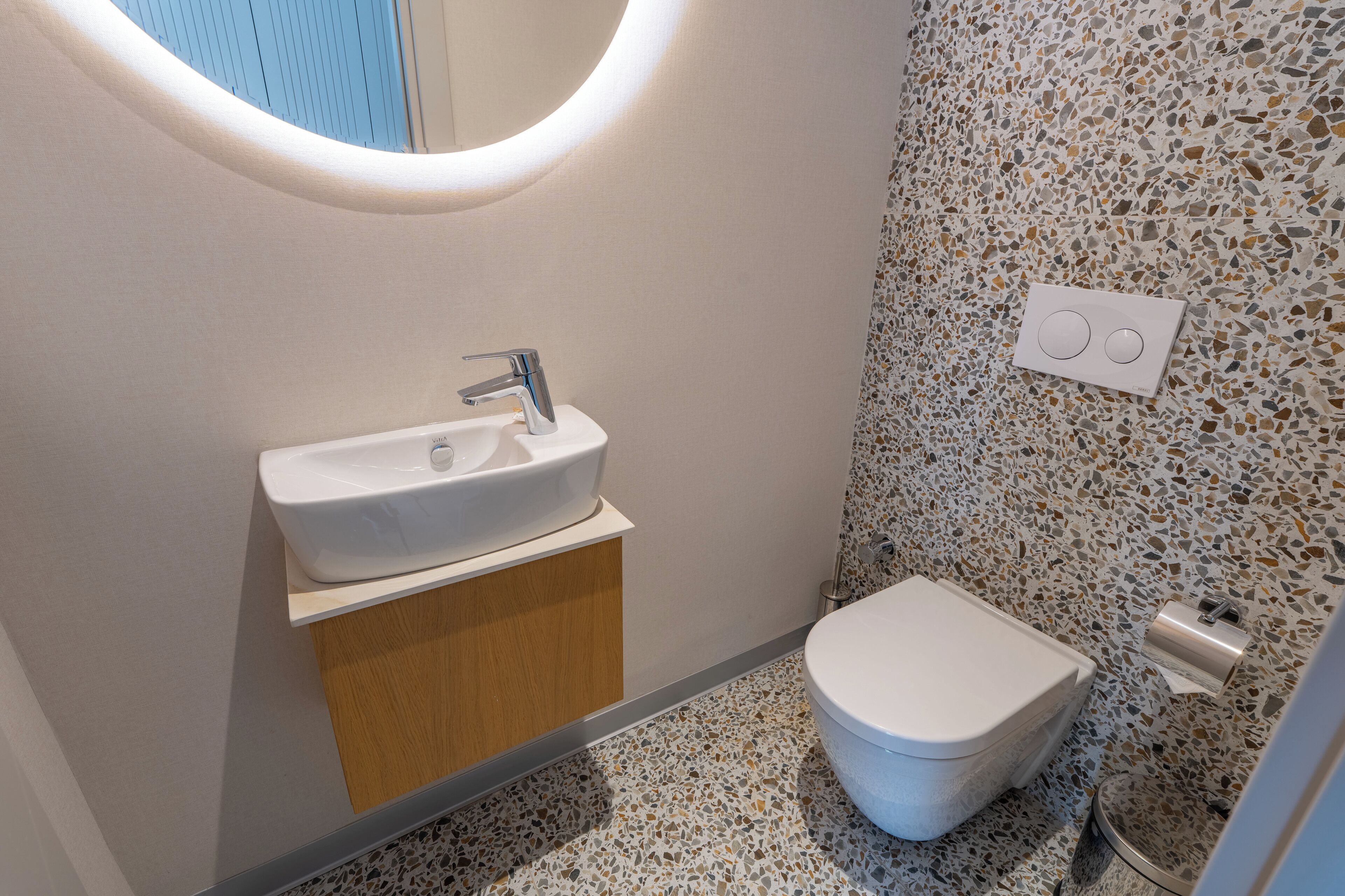 Casa de banho com lavatório branco, sanita e espelho fixado na parede.