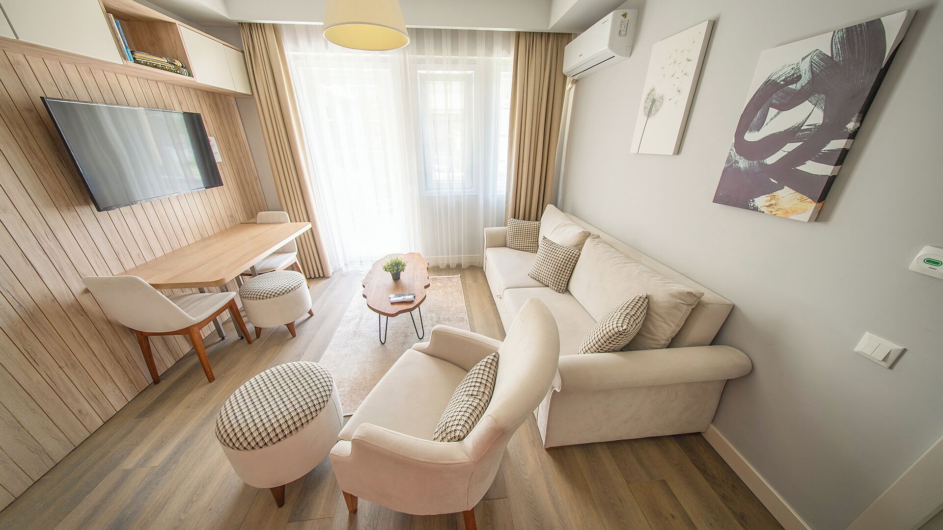 A modern living room with a sofa, armchairs, a dining table, and a TV mounted on the wall.