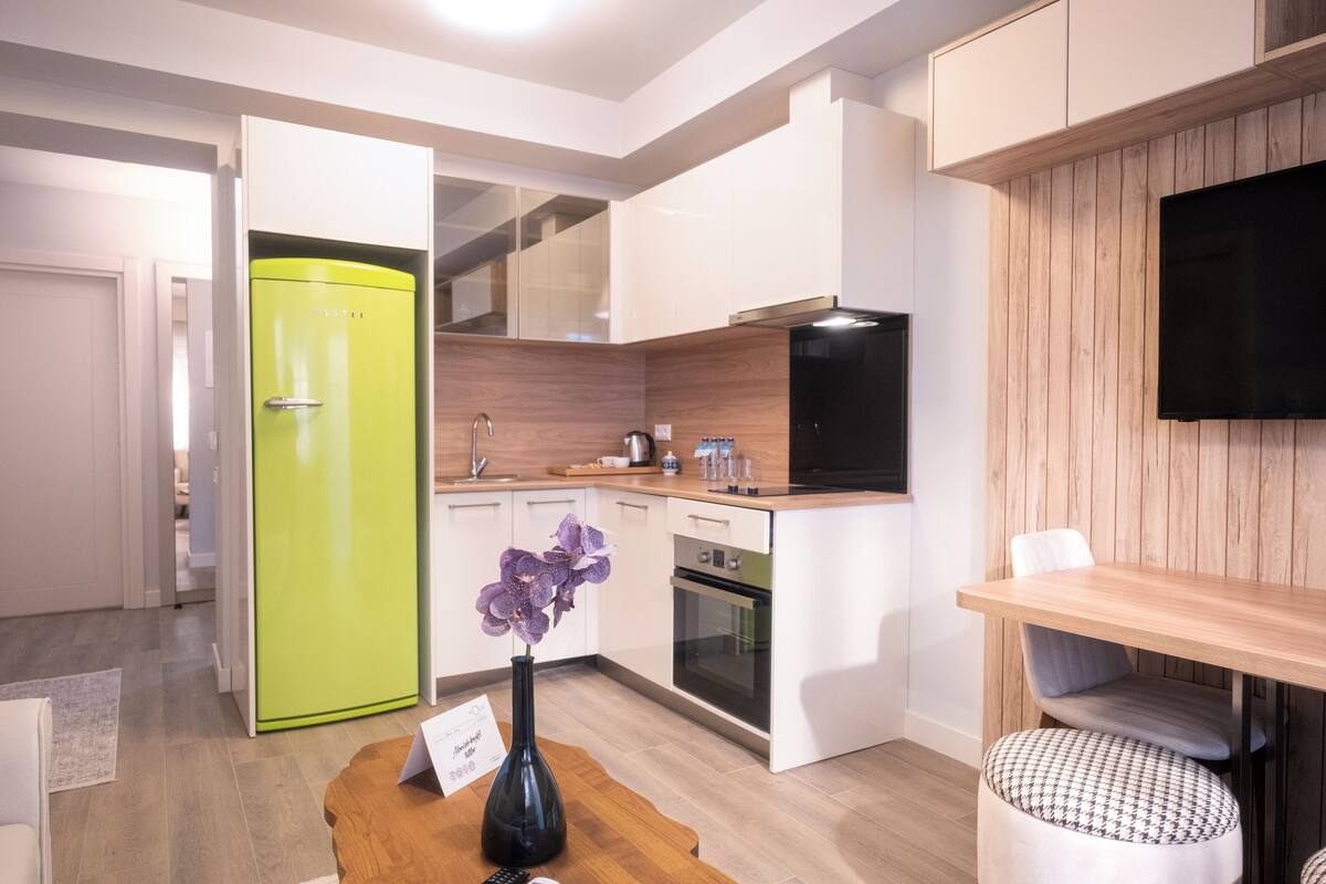 A modern kitchen with a green refrigerator, white cabinets, a wooden countertop, and a built-in oven.