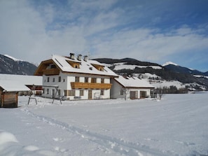 A snow-covered building with a balcony, surrounded by mountains and a clear sky.