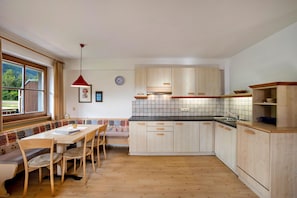 A kitchen with wooden cabinets, a tiled backsplash, a dining table with chairs, and a red pendant light.
