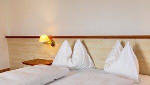 Habitación de hotel con cama, almohadas, mesita de noche y lámpara de pared.