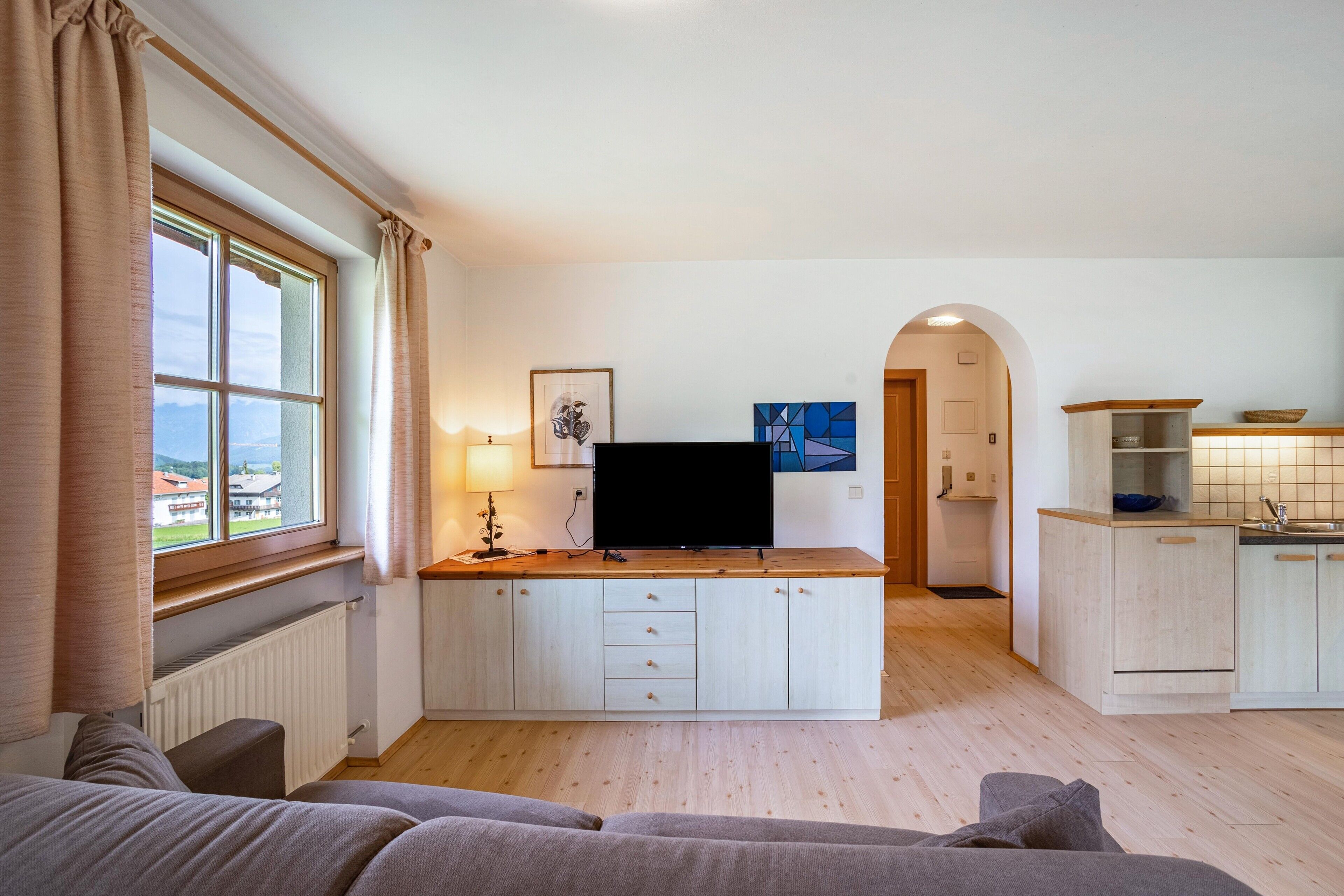 Un espacio habitable compacto con kitchenette, televisor, sofá y vistas al exterior.