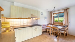 A kitchen with wooden cabinets, a tiled backsplash, a dining area with a table and chairs, and a window with curtains. - Apartment '2' with Mountain View, Shared Garden and Wi-Fi (Oberolang)
