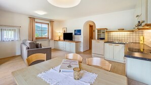 A modern living room with a sofa, a dining table with a book and a candle, a TV, and a kitchen area with cabinets and a sink. - Apartment '2' with Mountain View, Shared Garden and Wi-Fi (Oberolang)