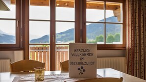 Une table avec un set de table, un verre et un panneau avec du texte, dans une pièce dotée de fenêtres en bois et offrant une vue sur les montagnes.