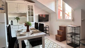 A compact kitchen with white cabinets, a dining table set for four, a TV mounted on the wall, and a small staircase leading to an upper level. - El Solsticio - 30601 (Somo)