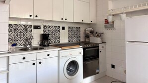 A compact kitchen with white cabinets, a washing machine, a coffee maker, and a stove. - El Solsticio - 30601 (Somo)
