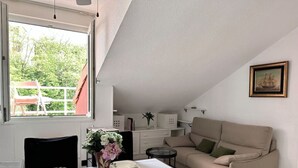 A dining area with a table set for four, a sofa, and a window with a view of greenery. - El Solsticio - 30601 (Somo)