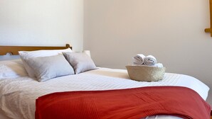Ein ordentlich bezogenes Bett mit roter Decke, zwei Kissen und einem Korb gefalteter Handtücher.