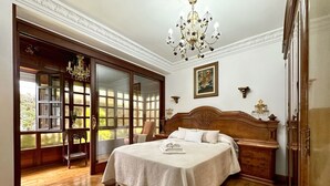 Un dormitorio con una cama grande, suelo de madera, un candelabro y un ventanal corredera que da a un balcón.