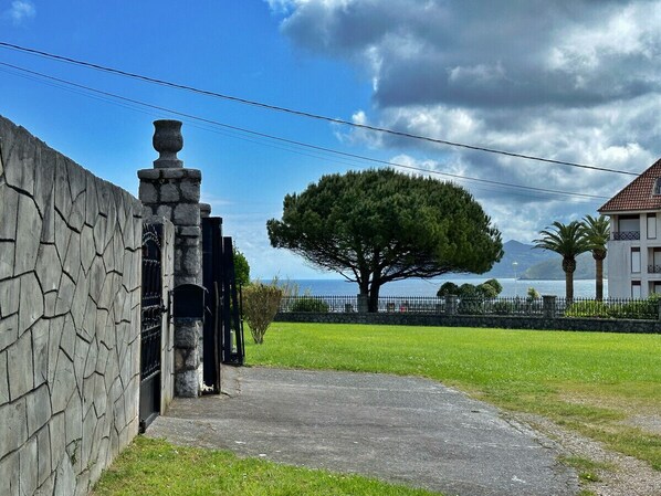 A stone wall with a gate, a large tree, and a building with a tiled roof in the background.