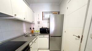 A compact kitchen with white cabinets, a stainless steel refrigerator, a microwave, and a sink.