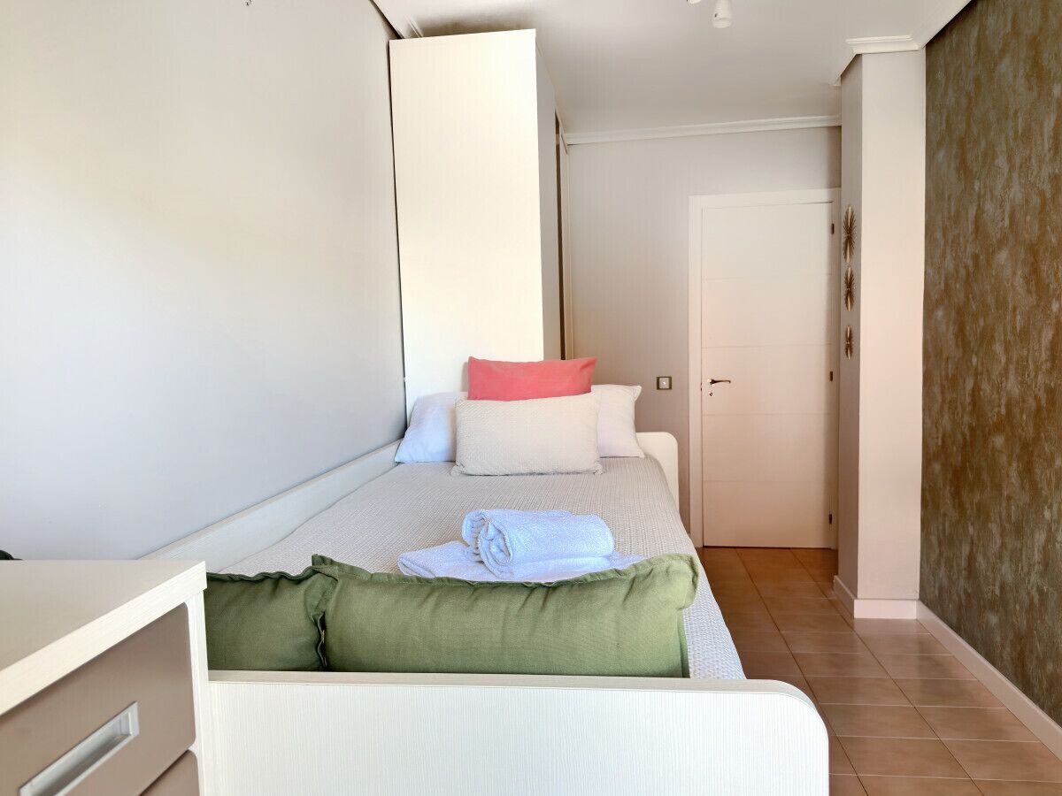 A bedroom with a bed, pillows, a green pillow, a white bedside table, and a door in the background.