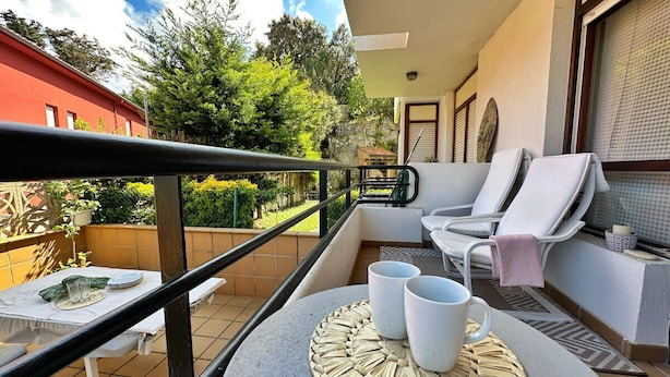 A balcony with a table set for two, two lounge chairs, and a small table with a white tablecloth.