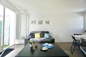 A modern living room with a sofa, a coffee table with cups and a tray, and a dining area with chairs.