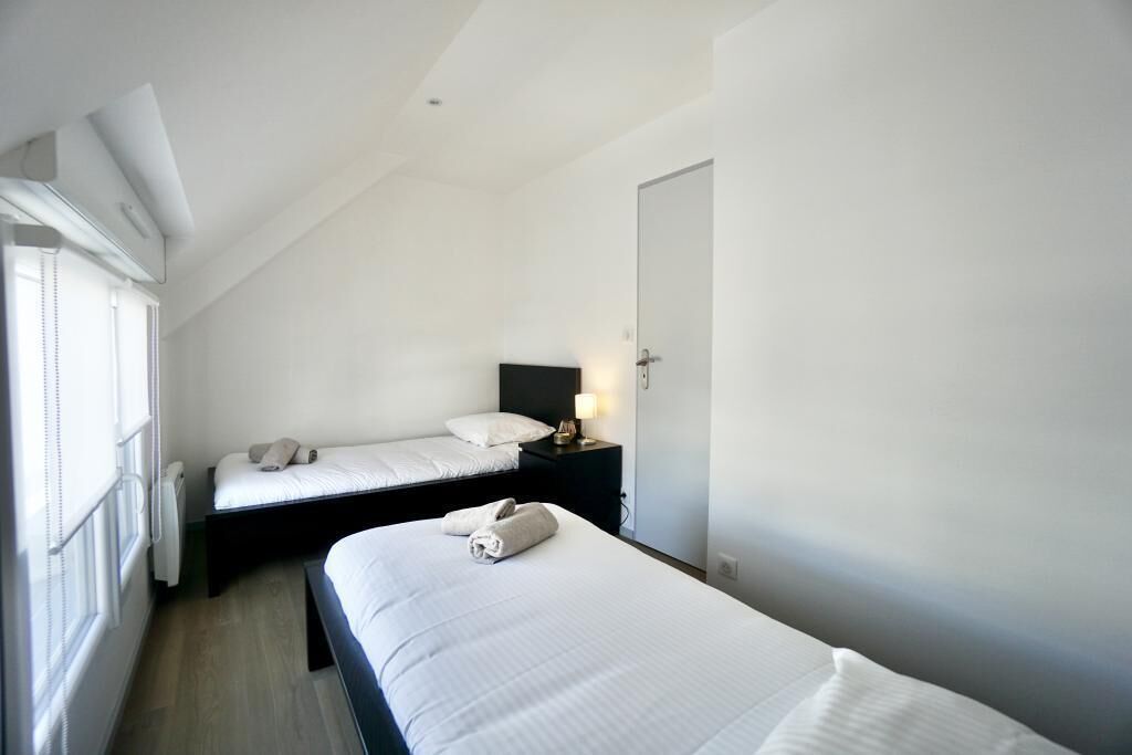 A hotel room with two single beds, a bedside table with a lamp, and a window with blinds.