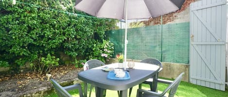 Un patio exterior con mesa y sillas, una sombrilla grande y un muro de jardín.