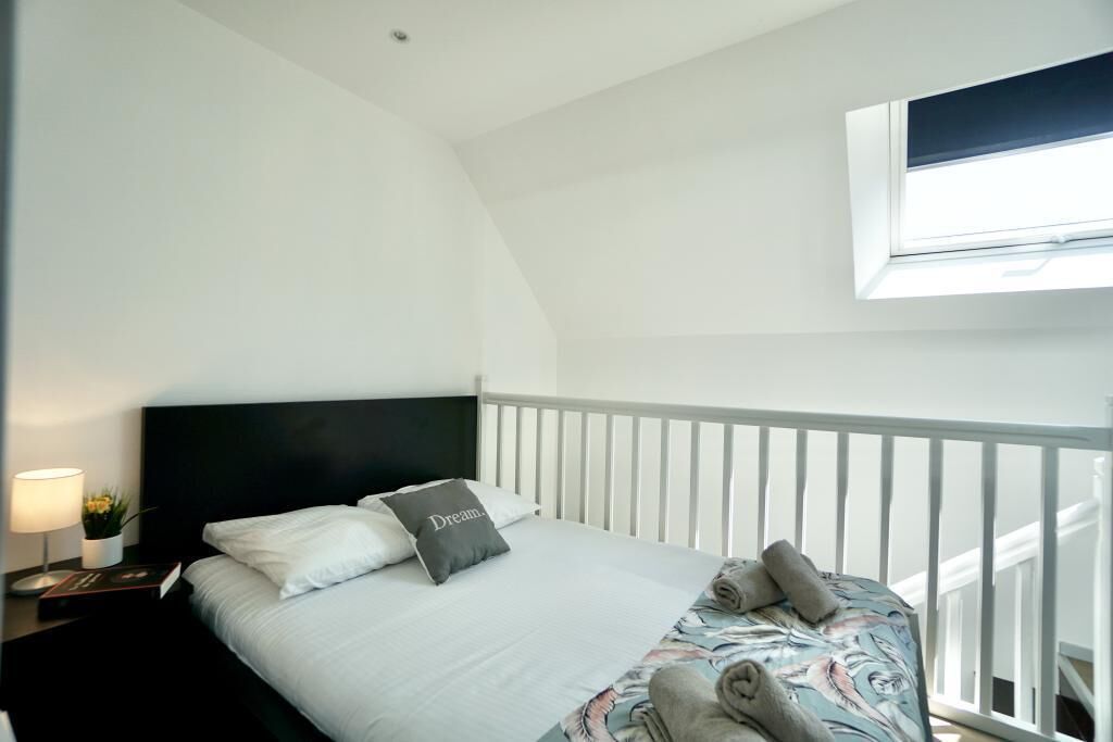 A bedroom with a bed, a nightstand, a lamp, and a window.