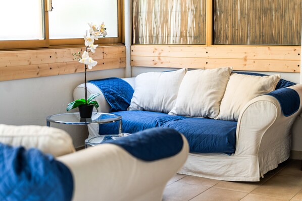 A room with a sofa, a small round table with a plant, and a window with wooden blinds.