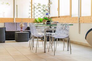 A modern dining area with a glass table, clear chairs, and a potted plant.