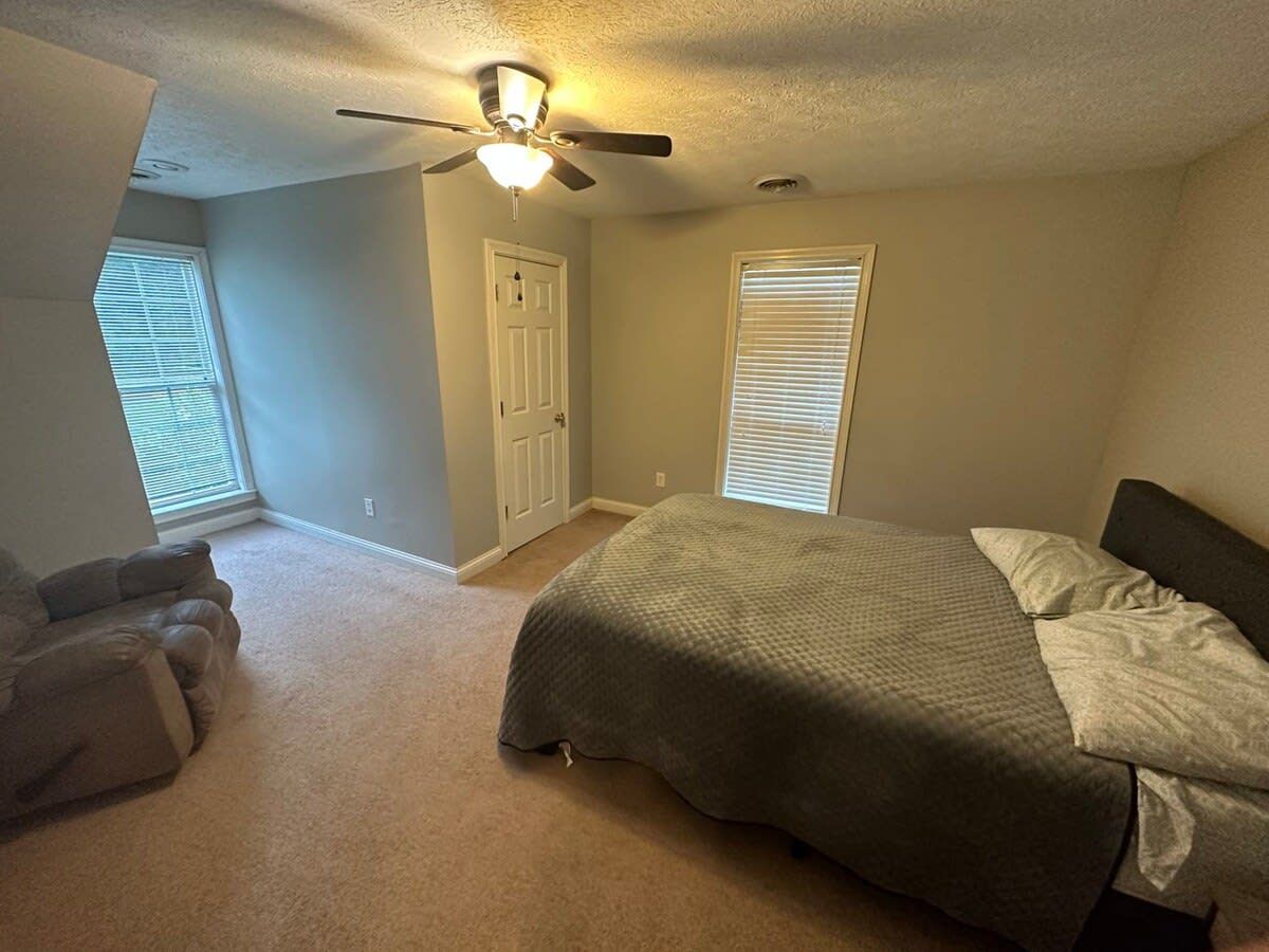 A bedroom with a bed, a ceiling fan, a door, and a window.